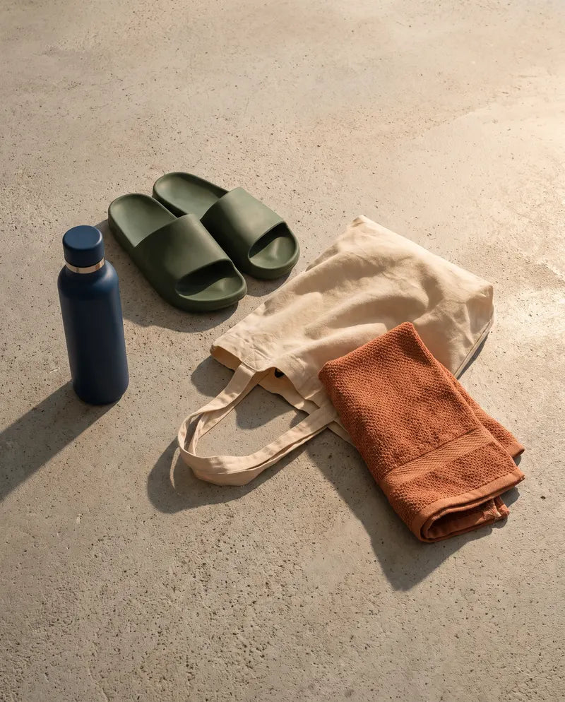 Stillleben mit Badelatschen, Tasche, Flasche und Handtuch auf Beton